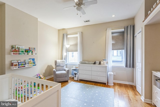 bedroom with a crib, light hardwood / wood-style flooring, and ceiling fan