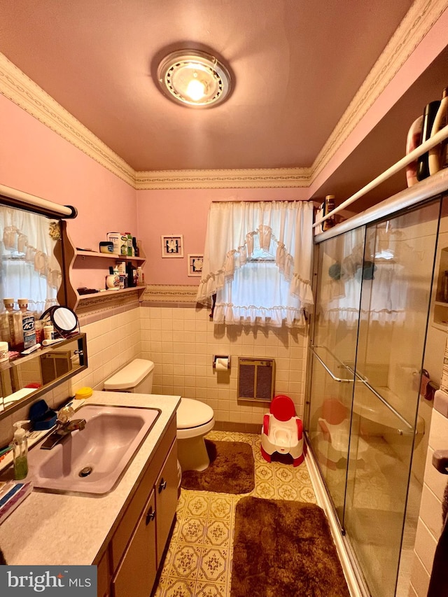 bathroom with tile walls, heating unit, vanity, toilet, and an enclosed shower