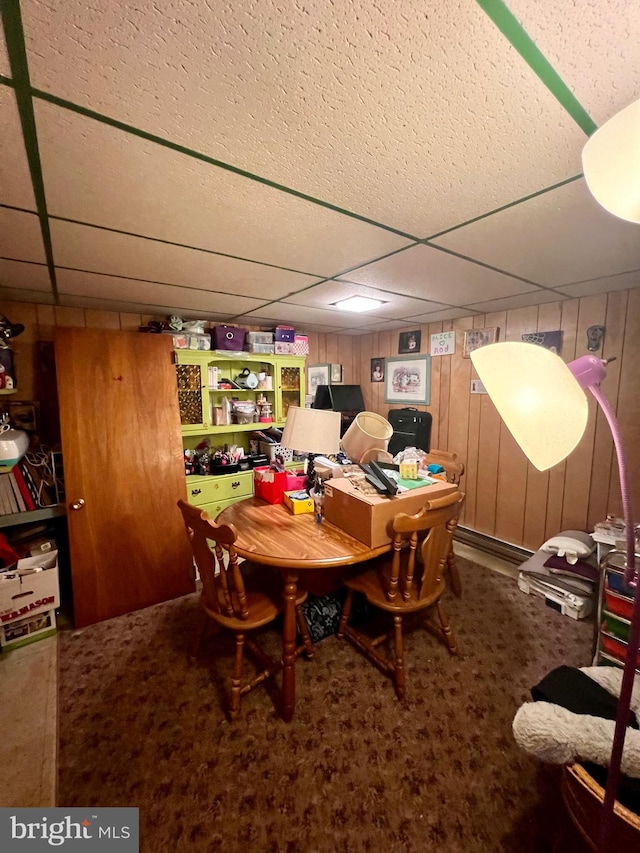 dining space featuring a paneled ceiling, carpet flooring, and wood walls