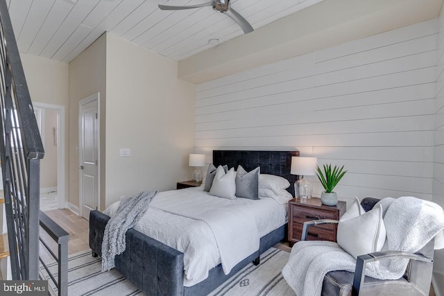 bedroom with ceiling fan, light wood-type flooring, wooden ceiling, and wooden walls