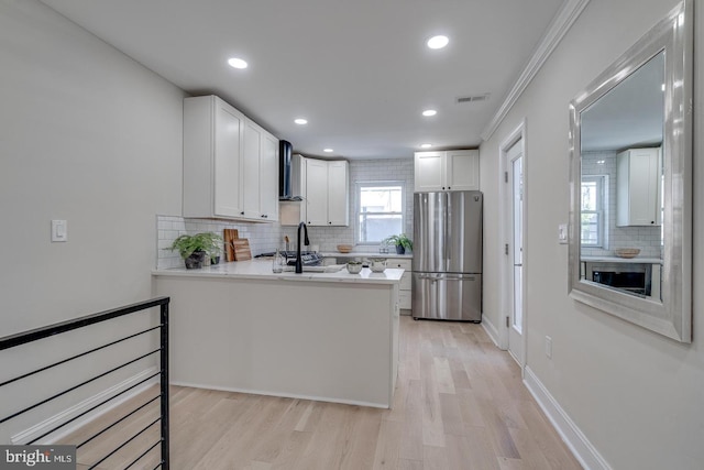 kitchen featuring kitchen peninsula, wall chimney exhaust hood, light hardwood / wood-style floors, white cabinetry, and stainless steel refrigerator