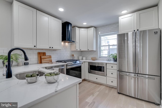 kitchen with white cabinetry, light stone countertops, stainless steel appliances, and wall chimney range hood