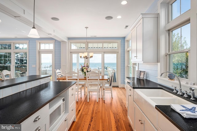 kitchen featuring light hardwood / wood-style flooring, white cabinets, plenty of natural light, and hanging light fixtures