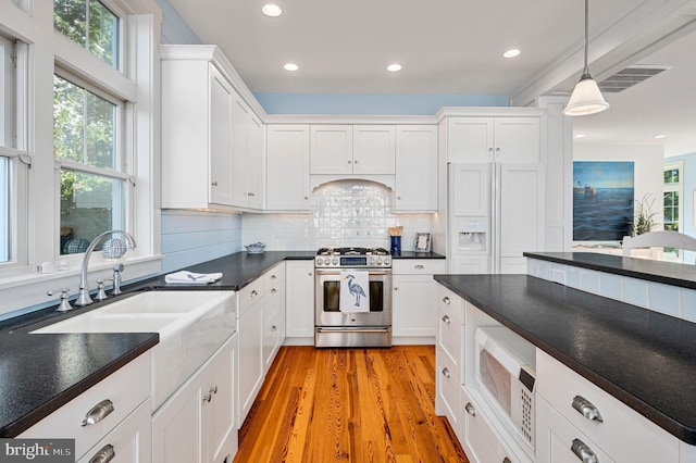 kitchen featuring light hardwood / wood-style floors, white cabinetry, white microwave, pendant lighting, and stainless steel range with gas cooktop