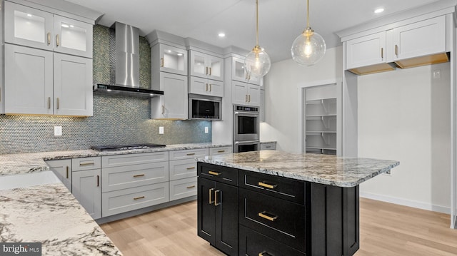 kitchen with stainless steel appliances, wall chimney range hood, pendant lighting, a kitchen island, and light wood-type flooring