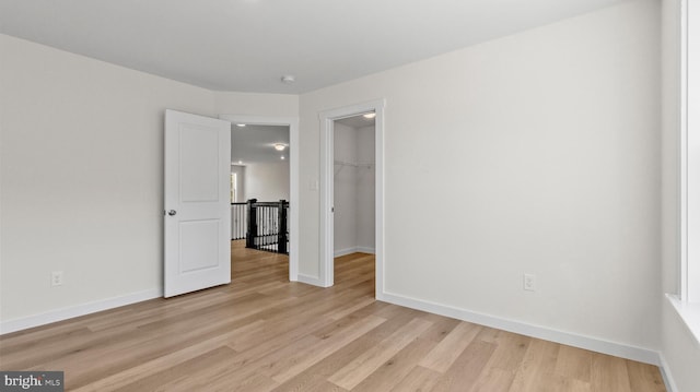 unfurnished bedroom with light wood-type flooring, a spacious closet, and a closet