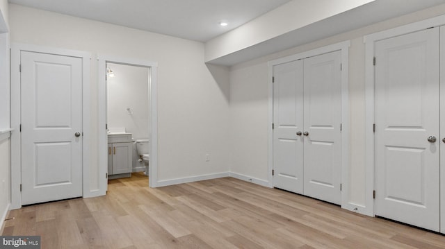 unfurnished bedroom with ensuite bath, light hardwood / wood-style floors, and two closets