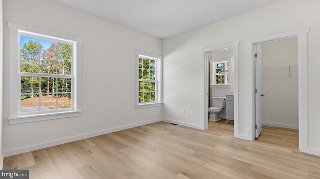 unfurnished bedroom featuring ensuite bathroom, light wood-type flooring, a spacious closet, and a closet