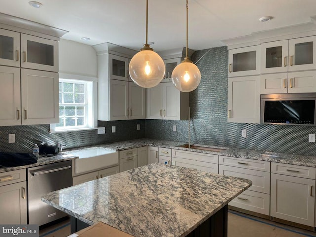 kitchen featuring light stone countertops, appliances with stainless steel finishes, tasteful backsplash, decorative light fixtures, and a center island