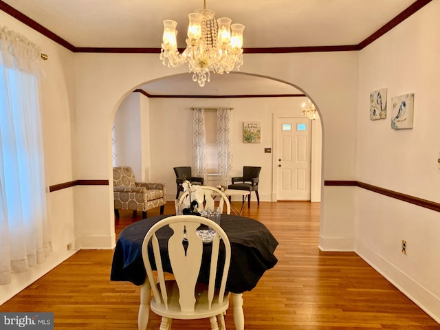 dining space with hardwood / wood-style flooring, crown molding, and an inviting chandelier