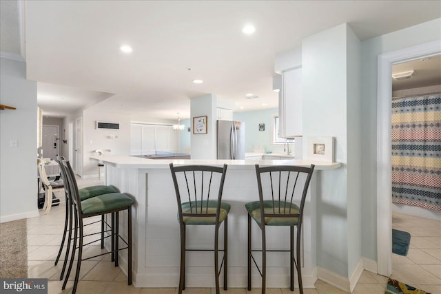 kitchen featuring a breakfast bar, white cabinetry, kitchen peninsula, stainless steel refrigerator, and light tile patterned floors