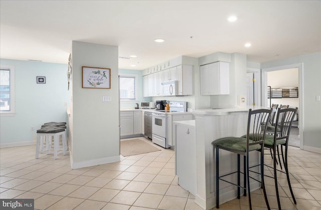 kitchen with a kitchen breakfast bar, white cabinets, white appliances, kitchen peninsula, and light tile patterned floors