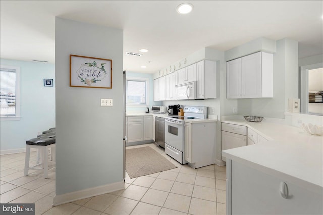 kitchen with white appliances, light tile patterned floors, white cabinetry, and a healthy amount of sunlight