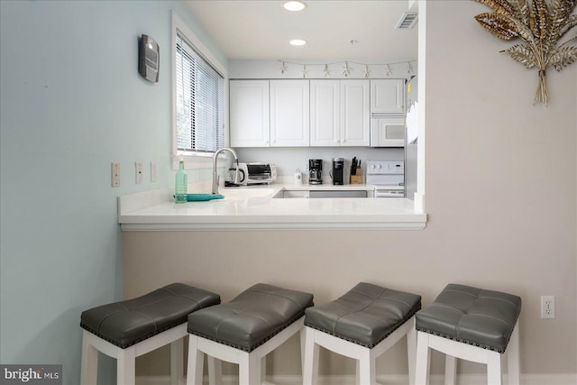 kitchen with white cabinets, white appliances, kitchen peninsula, a kitchen bar, and sink