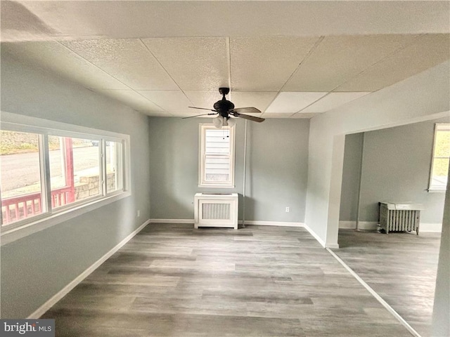 empty room with radiator, hardwood / wood-style floors, ceiling fan, and plenty of natural light