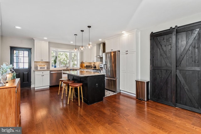 kitchen featuring a kitchen island, a barn door, dark hardwood / wood-style floors, stainless steel appliances, and decorative light fixtures