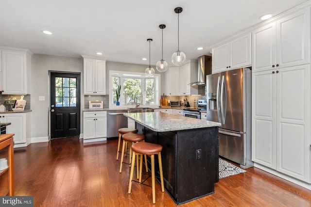 kitchen featuring wall chimney range hood, white cabinets, stainless steel appliances, and a kitchen island