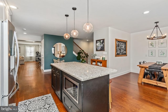 kitchen with dark hardwood / wood-style floors, stainless steel appliances, light stone countertops, a center island, and decorative light fixtures