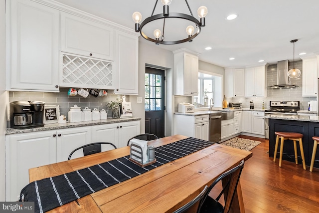 kitchen featuring wall chimney range hood, appliances with stainless steel finishes, white cabinetry, decorative light fixtures, and dark wood-type flooring