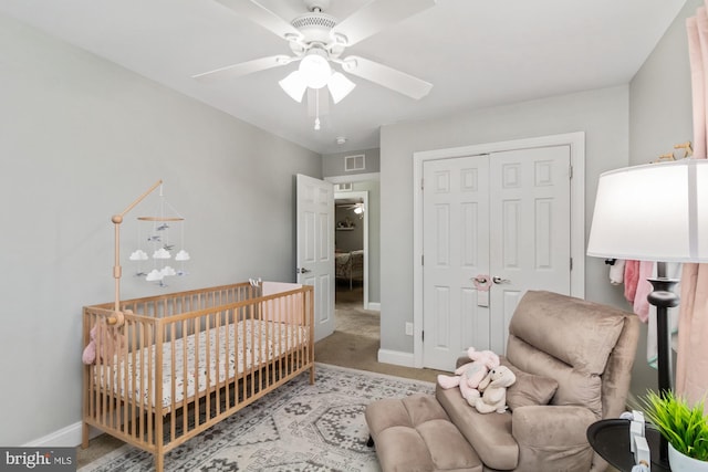 bedroom with a closet, ceiling fan, light carpet, and a crib