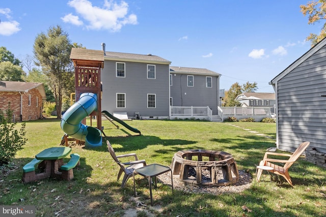 back of house featuring a lawn, a fire pit, and a playground