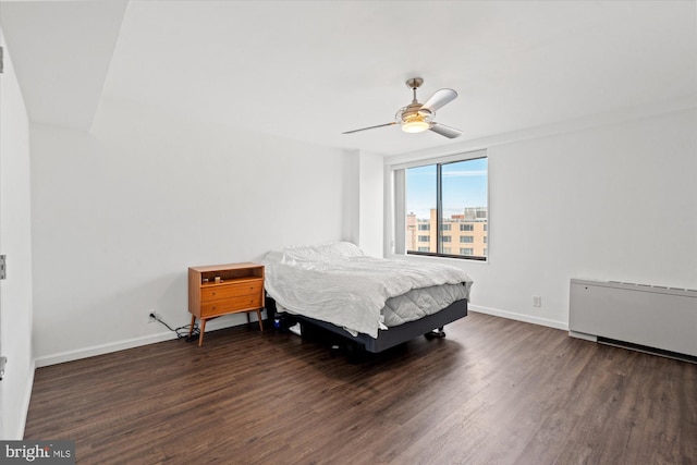 bedroom with dark wood-type flooring, ceiling fan, and radiator heating unit