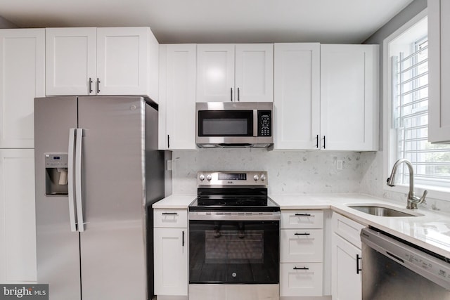 kitchen with decorative backsplash, white cabinetry, light stone counters, stainless steel appliances, and sink