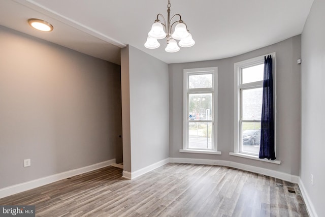 empty room featuring an inviting chandelier and hardwood / wood-style flooring