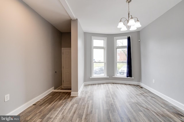 spare room featuring wood-type flooring and a chandelier