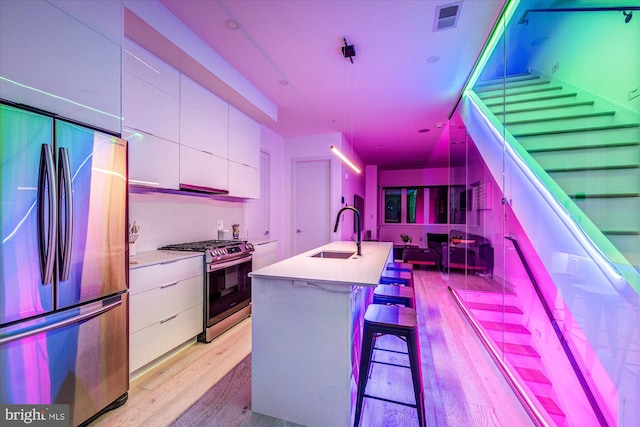 kitchen featuring white cabinetry, light hardwood / wood-style flooring, a center island with sink, appliances with stainless steel finishes, and decorative light fixtures