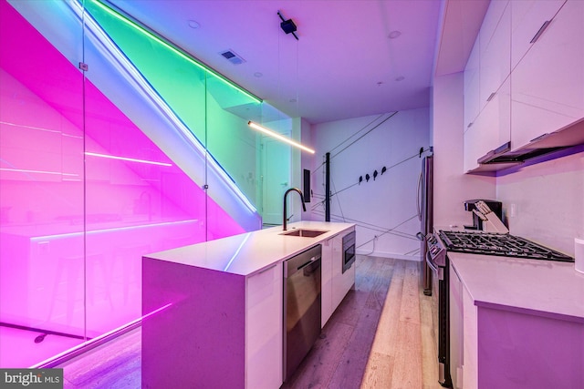 kitchen with stainless steel appliances, white cabinetry, light wood-type flooring, and sink