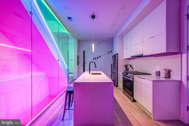 kitchen featuring pendant lighting, a kitchen island with sink, sink, light hardwood / wood-style flooring, and appliances with stainless steel finishes