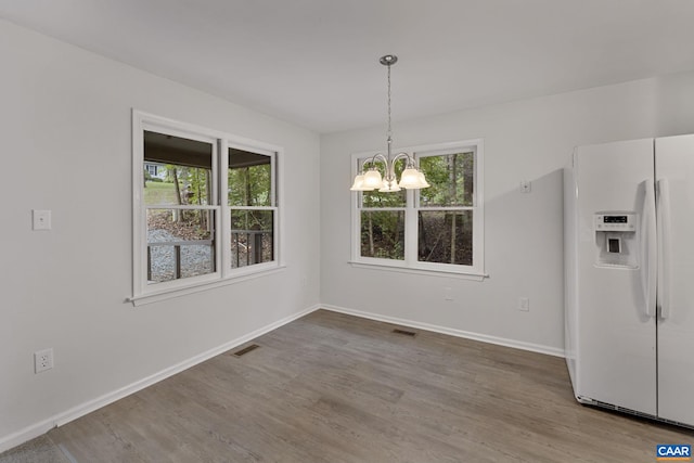 unfurnished dining area with wood-type flooring and an inviting chandelier