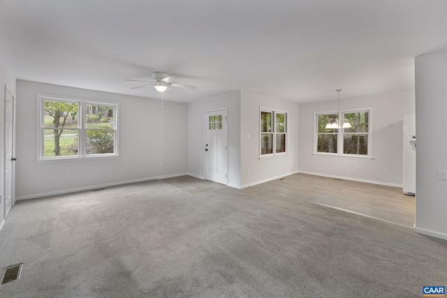 unfurnished living room with ceiling fan with notable chandelier, plenty of natural light, and light carpet