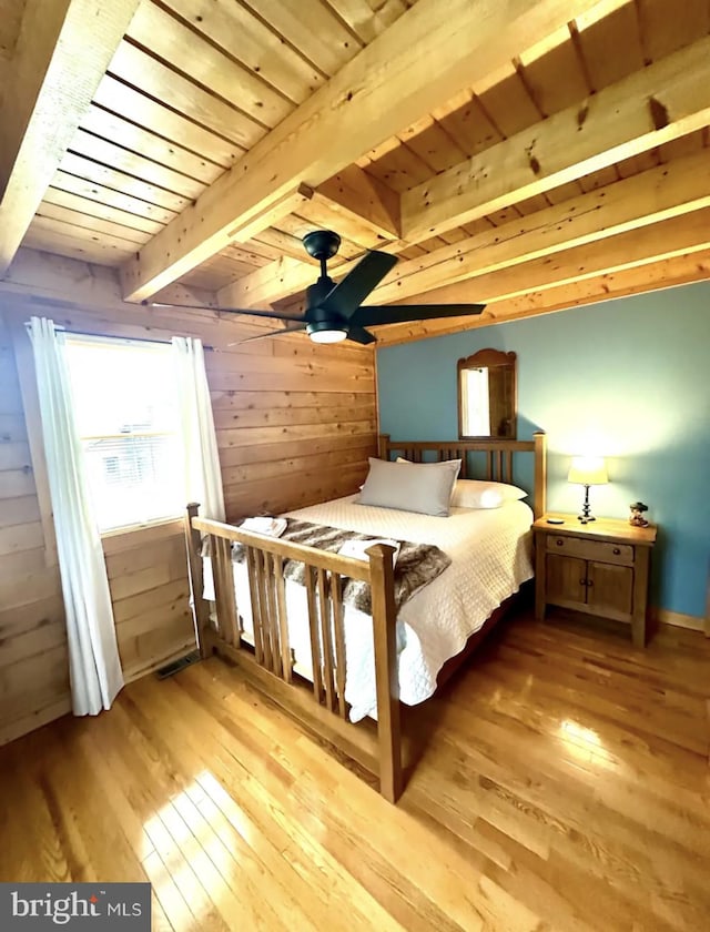 unfurnished bedroom with ceiling fan, beamed ceiling, wood walls, light hardwood / wood-style flooring, and wooden ceiling