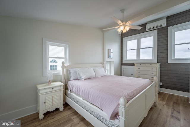 bedroom with wood-type flooring, vaulted ceiling, wooden walls, a wall mounted AC, and ceiling fan