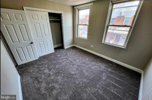 unfurnished bedroom with dark colored carpet, wooden walls, and a closet