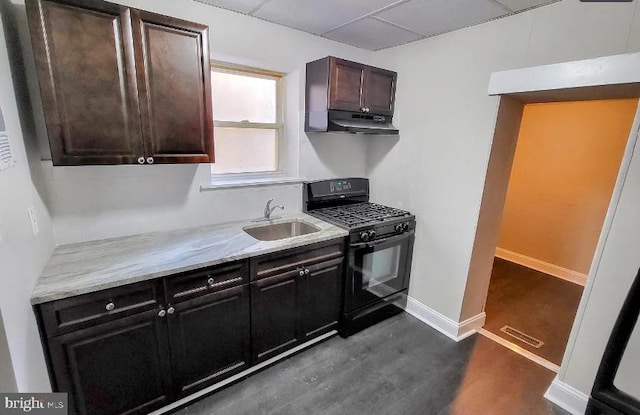 kitchen featuring black gas range, sink, light stone countertops, dark brown cabinets, and dark hardwood / wood-style flooring