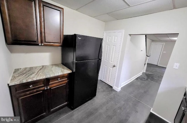 kitchen featuring a paneled ceiling, black refrigerator, and dark brown cabinets