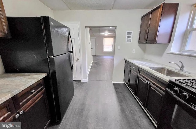 kitchen with stove, dark hardwood / wood-style flooring, a paneled ceiling, black fridge, and sink