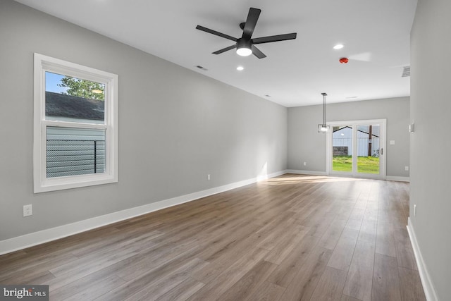 unfurnished room featuring a wealth of natural light, ceiling fan with notable chandelier, and light wood-type flooring