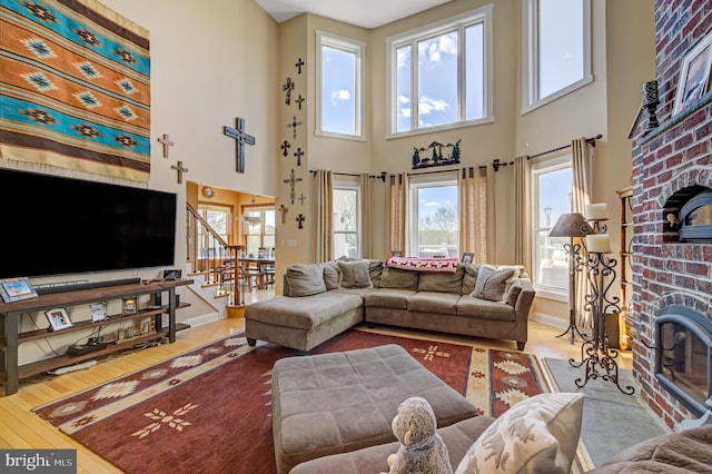 living room with a brick fireplace, wood-type flooring, a high ceiling, and a healthy amount of sunlight