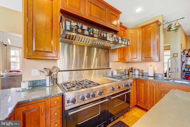 kitchen featuring high end range, sink, extractor fan, and light stone counters