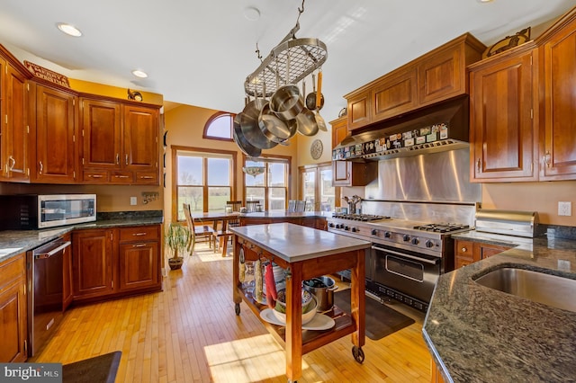 kitchen featuring appliances with stainless steel finishes, light hardwood / wood-style floors, dark stone countertops, and extractor fan