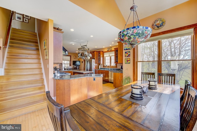 dining space with light hardwood / wood-style flooring, lofted ceiling, a notable chandelier, and sink