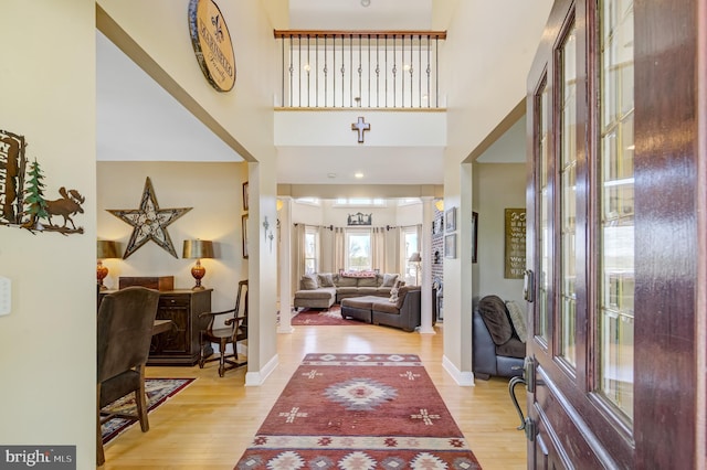 entrance foyer featuring decorative columns, a towering ceiling, and light hardwood / wood-style flooring