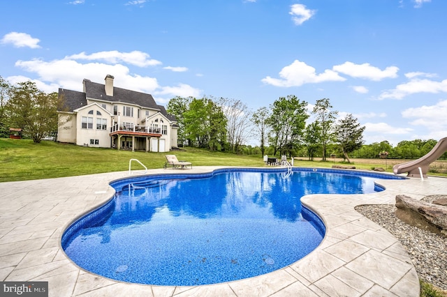 view of swimming pool featuring a wooden deck, a yard, a water slide, and a patio area