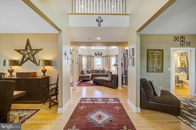 foyer featuring light wood-type flooring, decorative columns, and a high ceiling