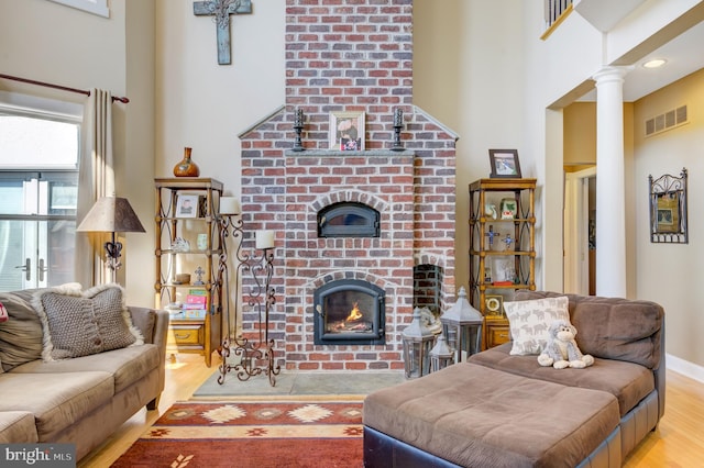 living room with light wood-type flooring, decorative columns, a fireplace, and a high ceiling