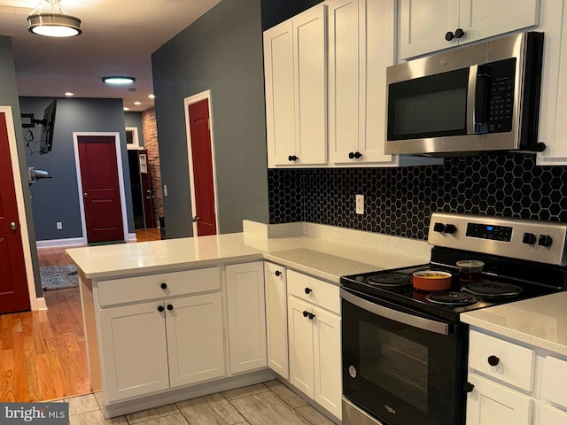 kitchen featuring light wood-type flooring, decorative backsplash, kitchen peninsula, appliances with stainless steel finishes, and white cabinetry